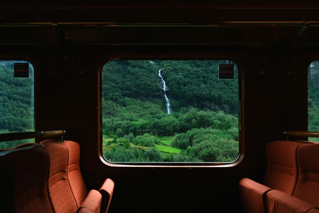 Ein grünes Tal mit Wasserfall, gesehen durch ein Zugfenster